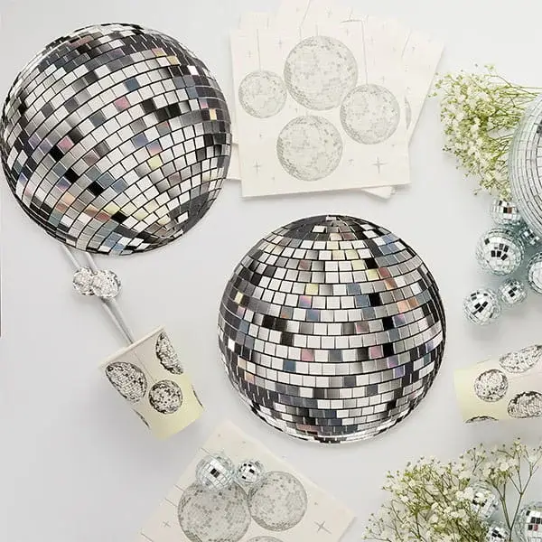 Disco-themed party setup with mirrored ball decorations, matching plates, cups, and silver party accents on a light background